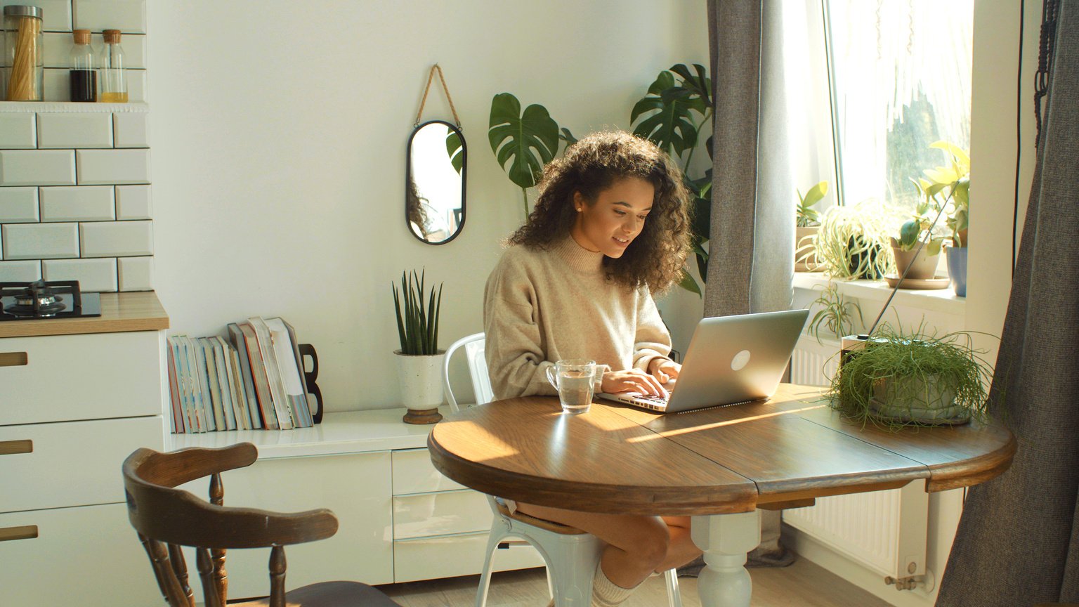 Charming young woman typing on laptop computer in a kitchen.